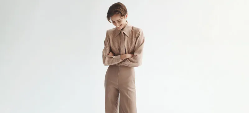 Model in Scanlan Theodore quiet luxury beige tailored suit, arms crossed, looking down on white background