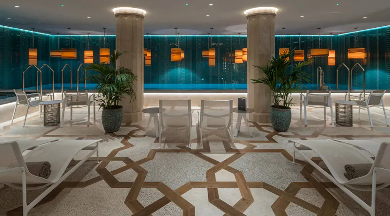 Elegant indoor pool at El Llorenç Parc de la Mar with teal walls, white loungers, potted palms, and geometric tile floor.