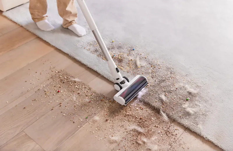 Person using Tineco PURE ONE S15 Pro cordless stick vacuum to clean pet hair and debris from carpet in modern home.
