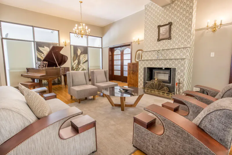 Elegant hotel lounge with grand piano, gray armchairs, glass coffee table, and ornate fireplace.