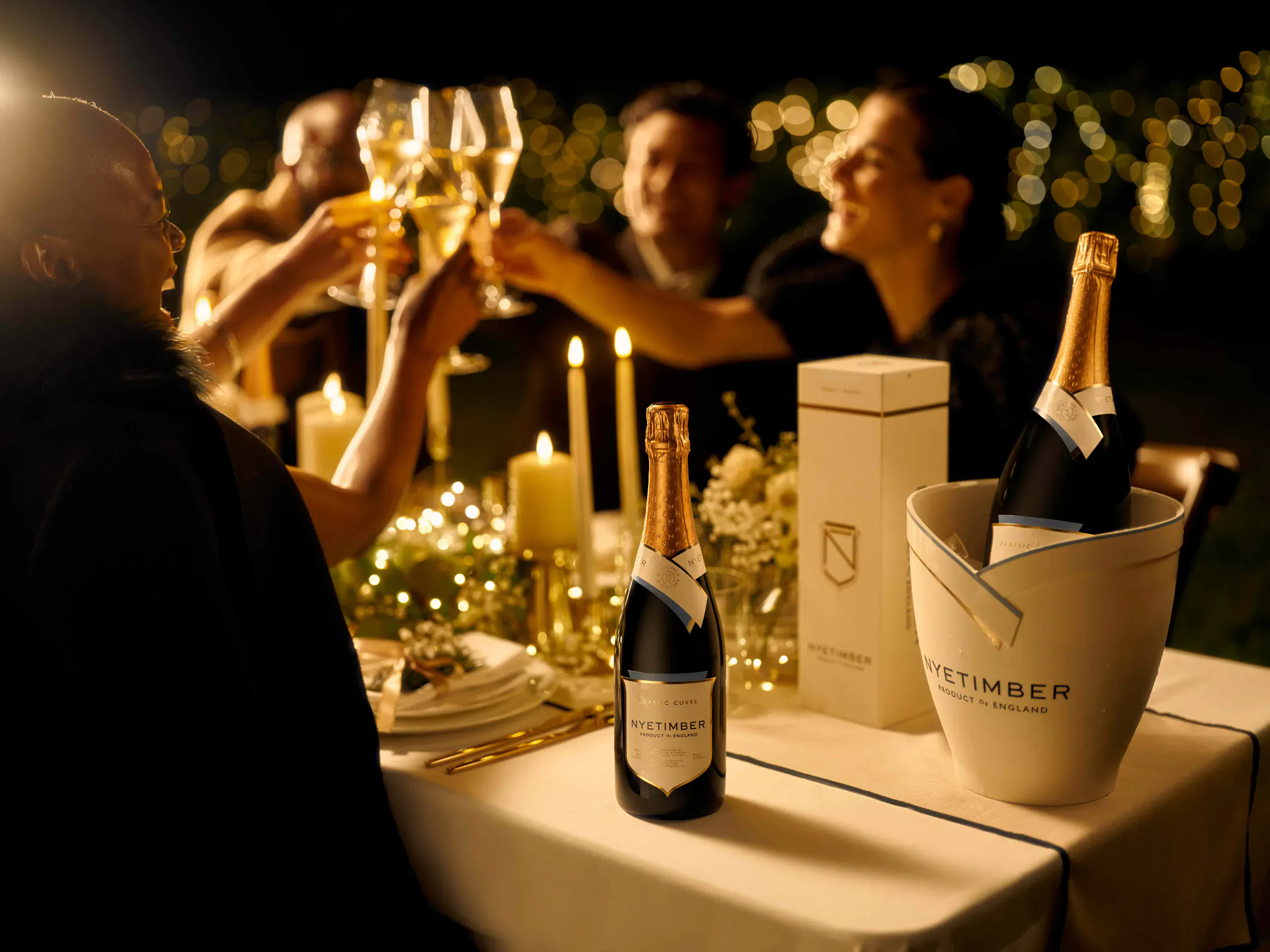 Group outdoors at night toasting with Nyetimbeer champagne flutes and bottles, candles and Christmas lights on table