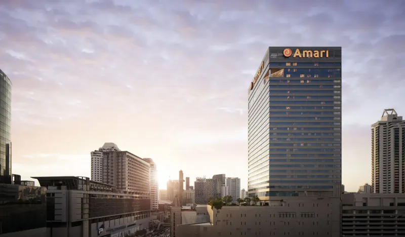 Amari Bangkok hotel towering in city skyline at sunset, with 'Amari' logo on building amid modern towers.