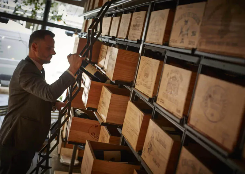 Man in suit climbs ladder to reach stacked wooden wine crates in 28-50 Oxford Circus wine gallery