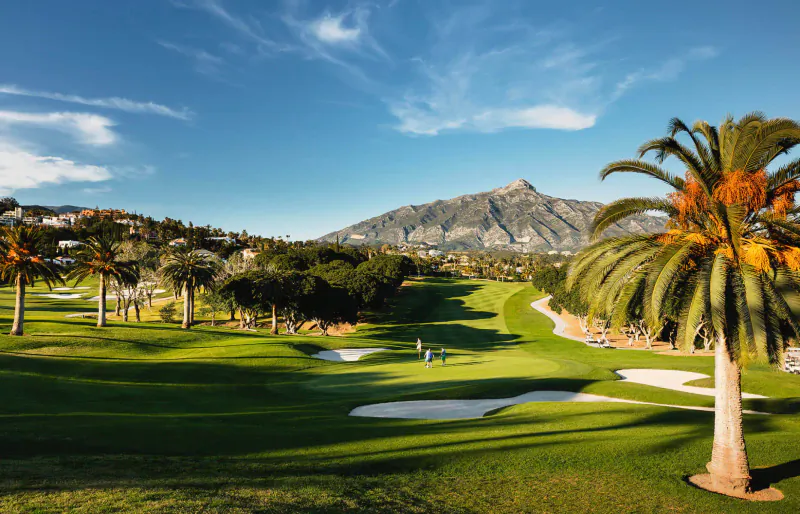 Los Naranjos Golf Club in Marbella: lush green fairways, palm trees, bunkers, distant La Concha mountain under blue sky.