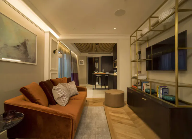 Cozy lounge in The Guardsman boutique London hotel with orange velvet sofa, gold shelves, bar, and warm lighting.