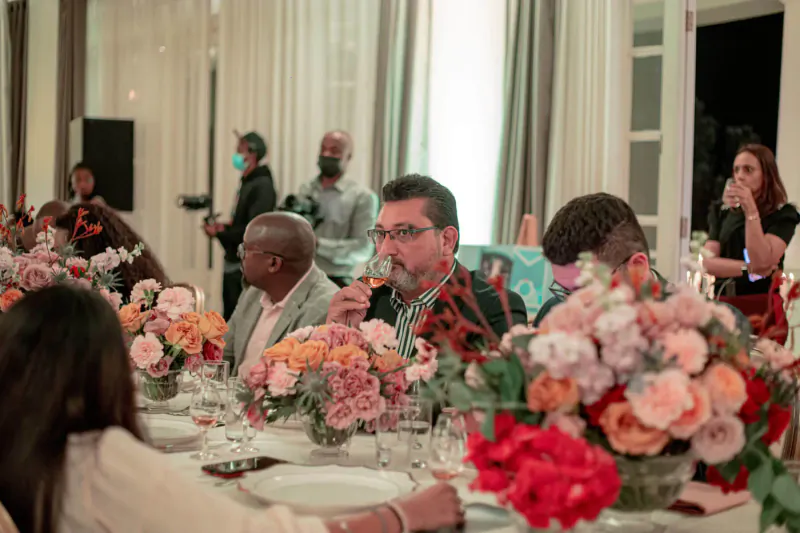 Glenfiddich celebrity event in gallery: diverse guests in masks sipping drinks at flower-adorned table.