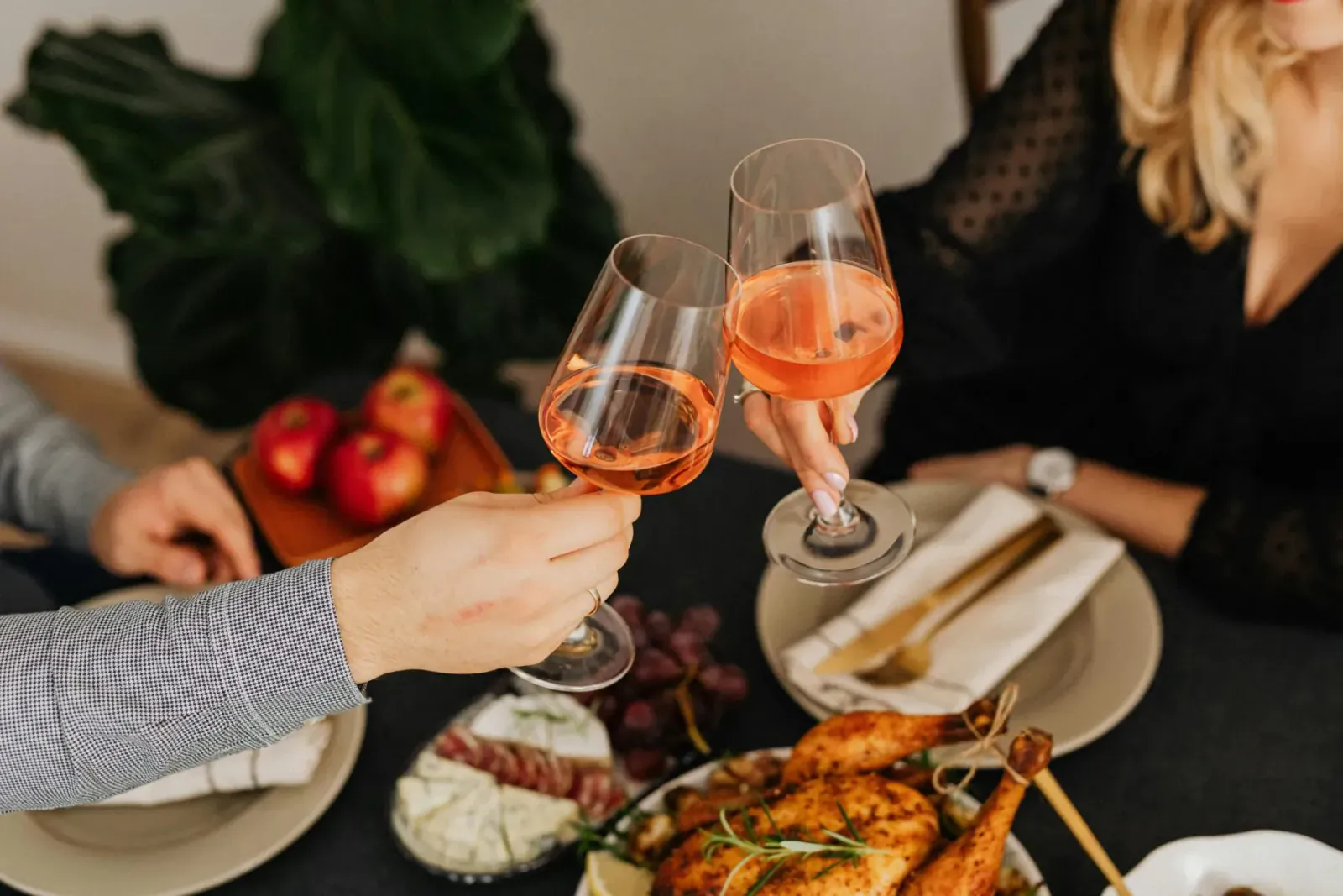 Couple toasting with orange wine glasses over dinner table with roast chicken, grapes, and apples