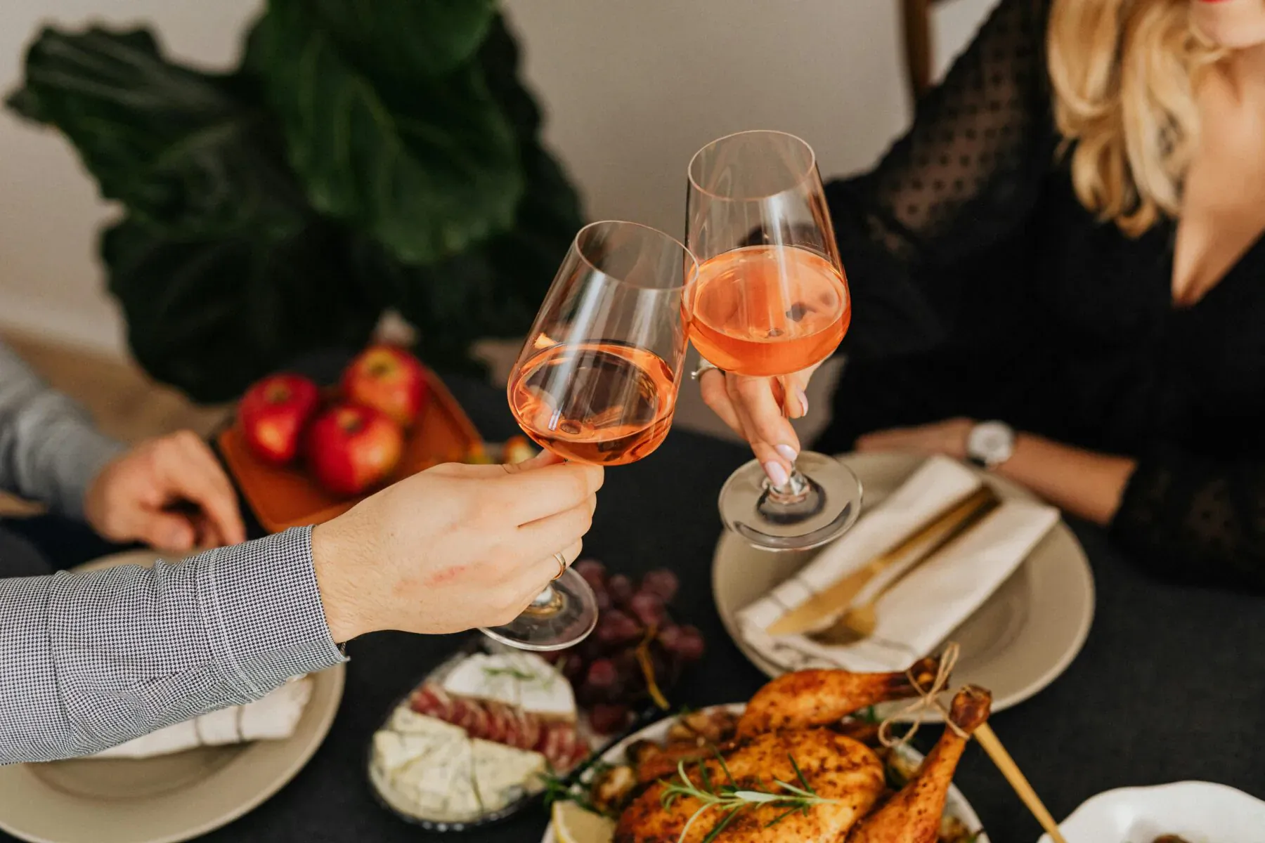 Couple toasting with orange wine glasses over dinner table with roast chicken, grapes, and apples