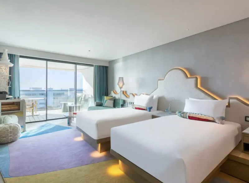 Spacious W Algarve hotel room with two white beds, colorful rugs, balcony overlooking ocean.