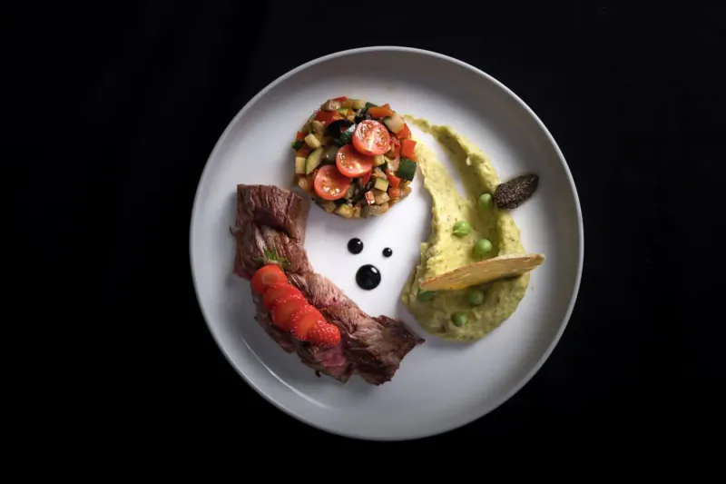 Round white plate with sliced beef, pea puree, tomato salsa, and veggie relish on black background
