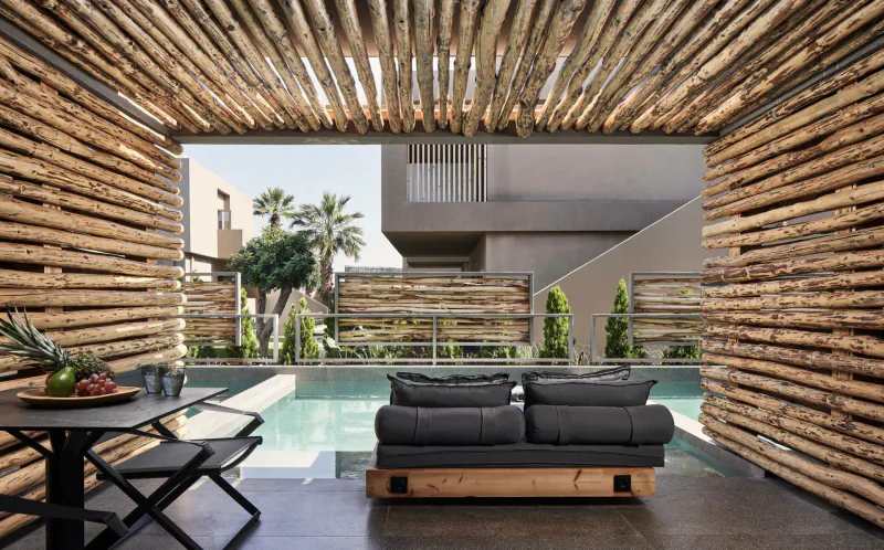 Open bamboo pavilion at Elysium Boutique Hotel with gray sofa, table of fruit, infinity pool, palms, and sea view