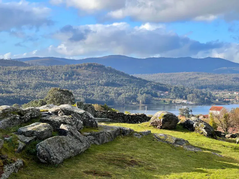 Rocky outcrop overlooking forested mountains, lake, and village at Terranam Wellness Retreat under partly cloudy sky