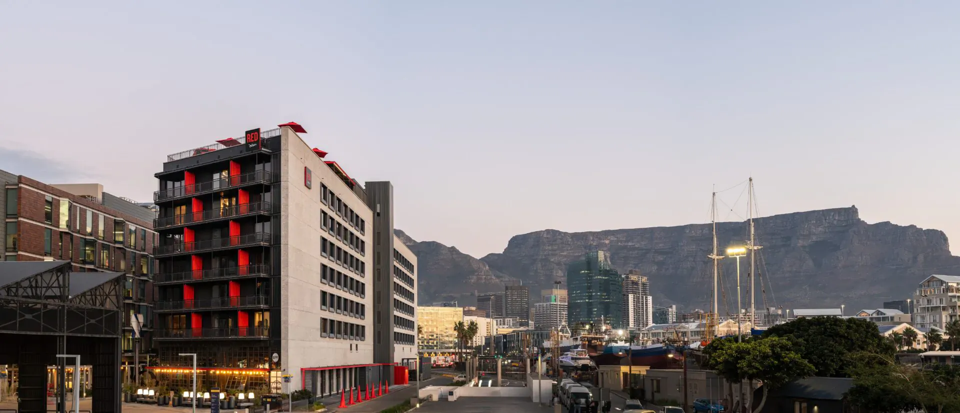 Radisson Red hotel with red accents at V&A Waterfront, Cape Town, Table Mountain in twilight skyline.