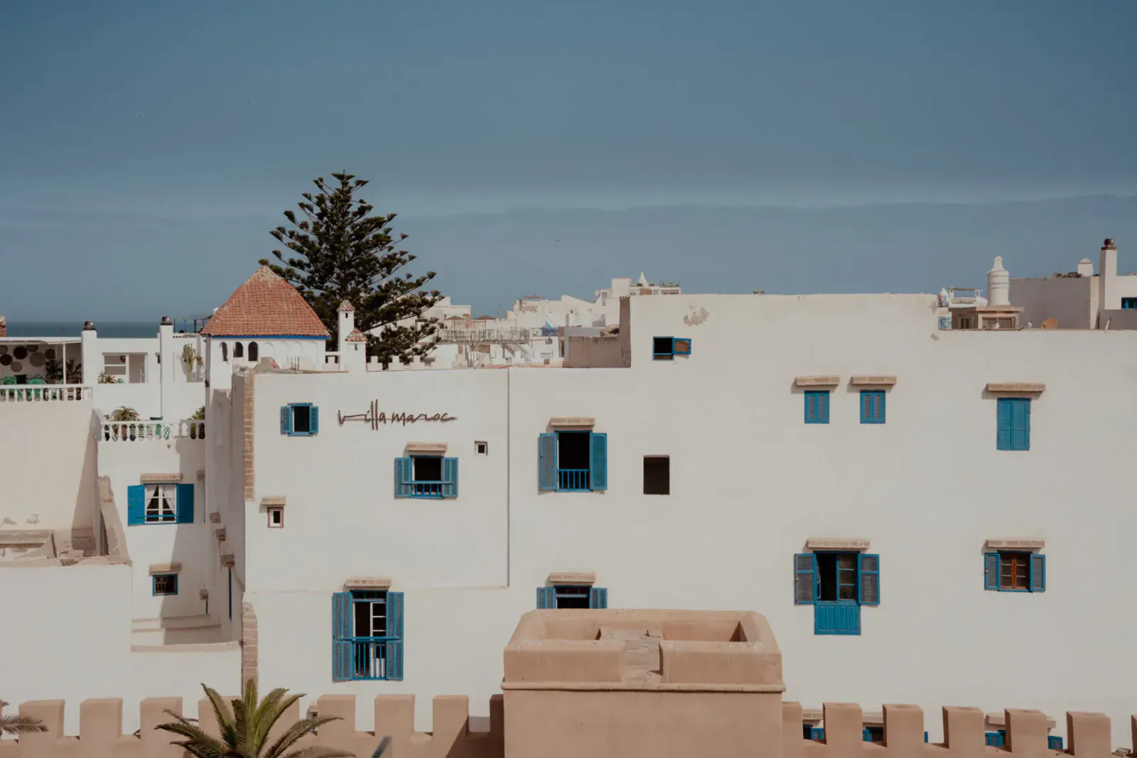 White-washed buildings with blue shutters and palm trees in Essaouira, Morocco, under clear blue sky