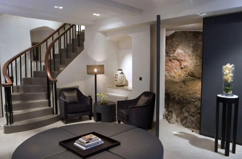Elegant Roch Castle hotel interior with curved staircase, black leather armchairs, round table with books, rock wall, vase of flowers.