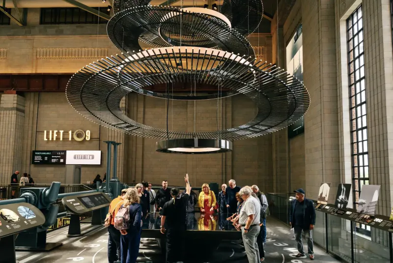 Visitors admire large hanging ring sculptures under 'LIFT 109' sign in grand Battersea Power Station hall.