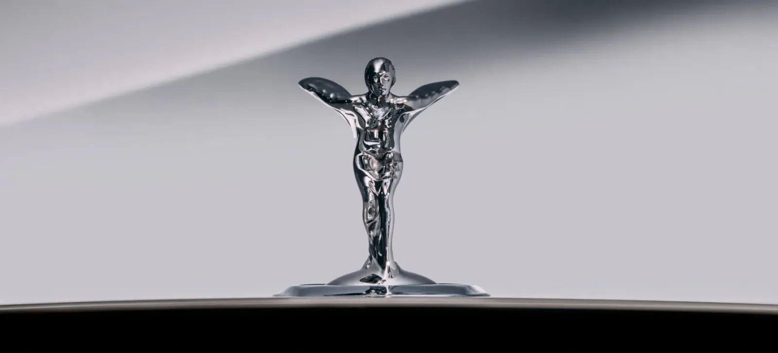 Redesigned Spirit of Ecstasy hood ornament on aerodynamic Rolls-Royce, chrome figure with outstretched wings