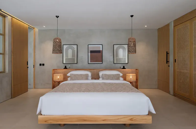 Modern wooden bed with white sheets and bedside lamps in minimalist resort bedroom with rattan pendants and abstract art.