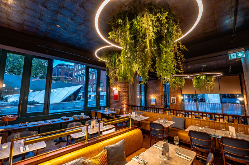 Amalfi Ristorante interior: stylish dining area with hanging plants, wooden tables, leather booths, large windows overlooking city.