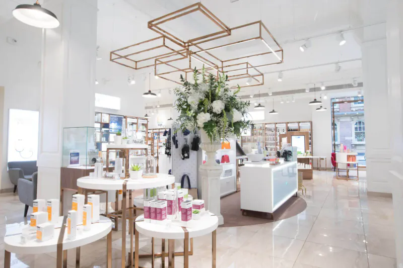 Modern luxury cosmetics store interior with white displays, skincare products, and large floral installation.