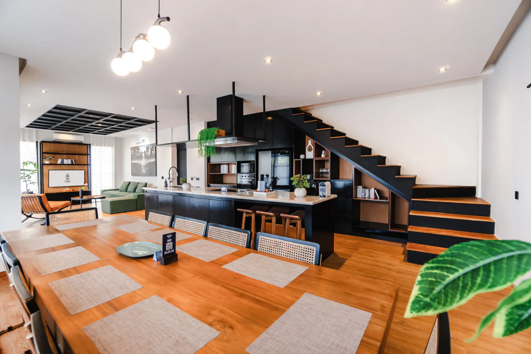 Spacious modern open-plan kitchen and living area with black island, stairs, plants, and wooden floors in luxury Bali villa