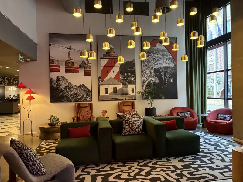 Modern hotel lobby at Radisson Red V&A Waterfront with green modular sofas, pendant lights, mountain artwork, and geometric rug.