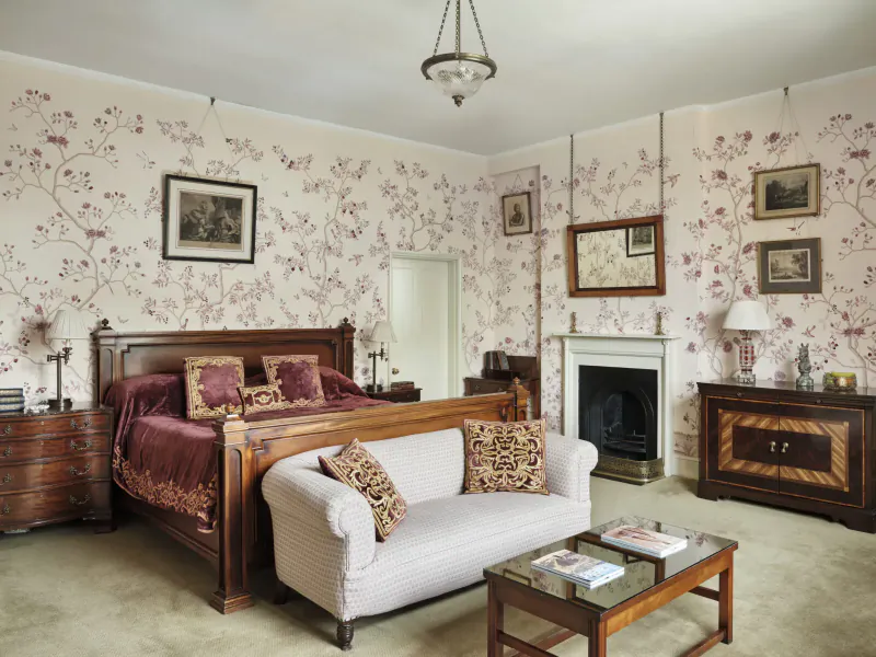 Elegant Edwardian bedroom in Home House club with floral wallpaper, wood bed, velvet bedding, sofa, and coffee table.