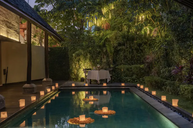 Twilight pool at Ametis Villa Bali with floating candles, lush tropical garden, lit table, and luxury villa backdrop
