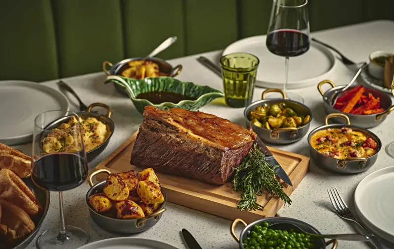 Roast beef on wooden board with roasted potatoes, peas, olives, and red wine at elegant brasserie table