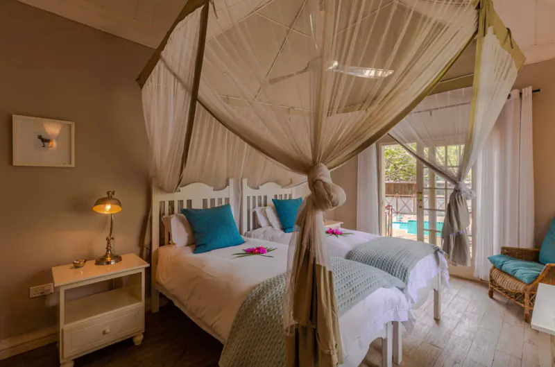 Cozy bedroom with white canopy bed, turquoise pillows, lamp, and pool view through French doors at The River Club.