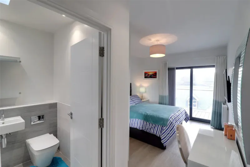 Bright Woolacombe Bay hotel room with teal bed, en-suite bathroom, desk, and balcony view.