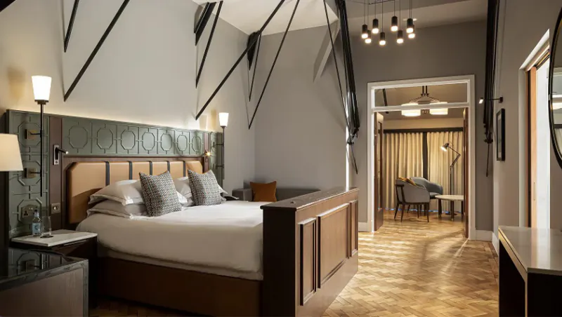 Elegant hotel bedroom at The Parkgate Hotel Cardiff with wooden king bed, high ceilings, lamps, and adjacent lounge area.