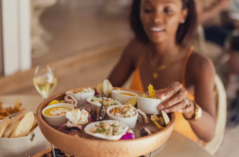 Woman at Catherine’s Café Sur La Plage in Antigua smiling while holding lemon over seafood platter with oysters, clams, and white wine