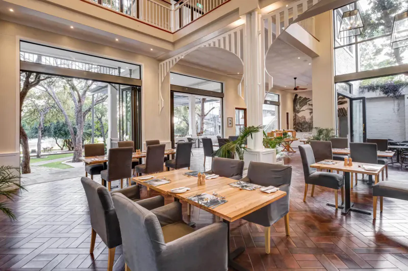 Elegant dining room at Palm River Hotel with wooden tables, chairs, plants, and garden views near Victoria Falls.