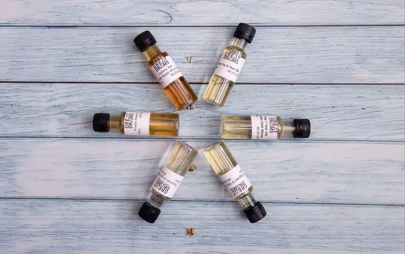 Six small independent whisky sample bottles arranged in a circle on blue wood, with labels and a small emblem.