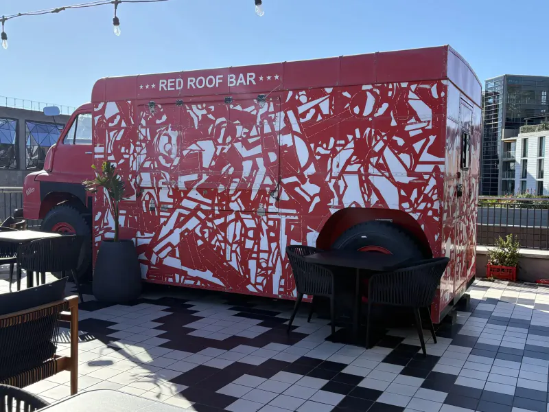 Red Roof Bar food truck with geometric patterns parked on rooftop terrace with tables and chairs, Cape Town.