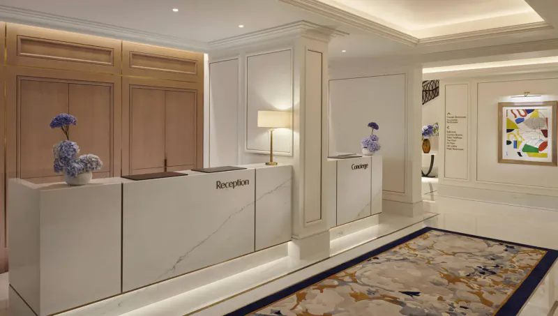 Elegant Carlton Tower Jumeirah hotel reception desk with blue floral vases, columns, artwork, and carpeted floor.