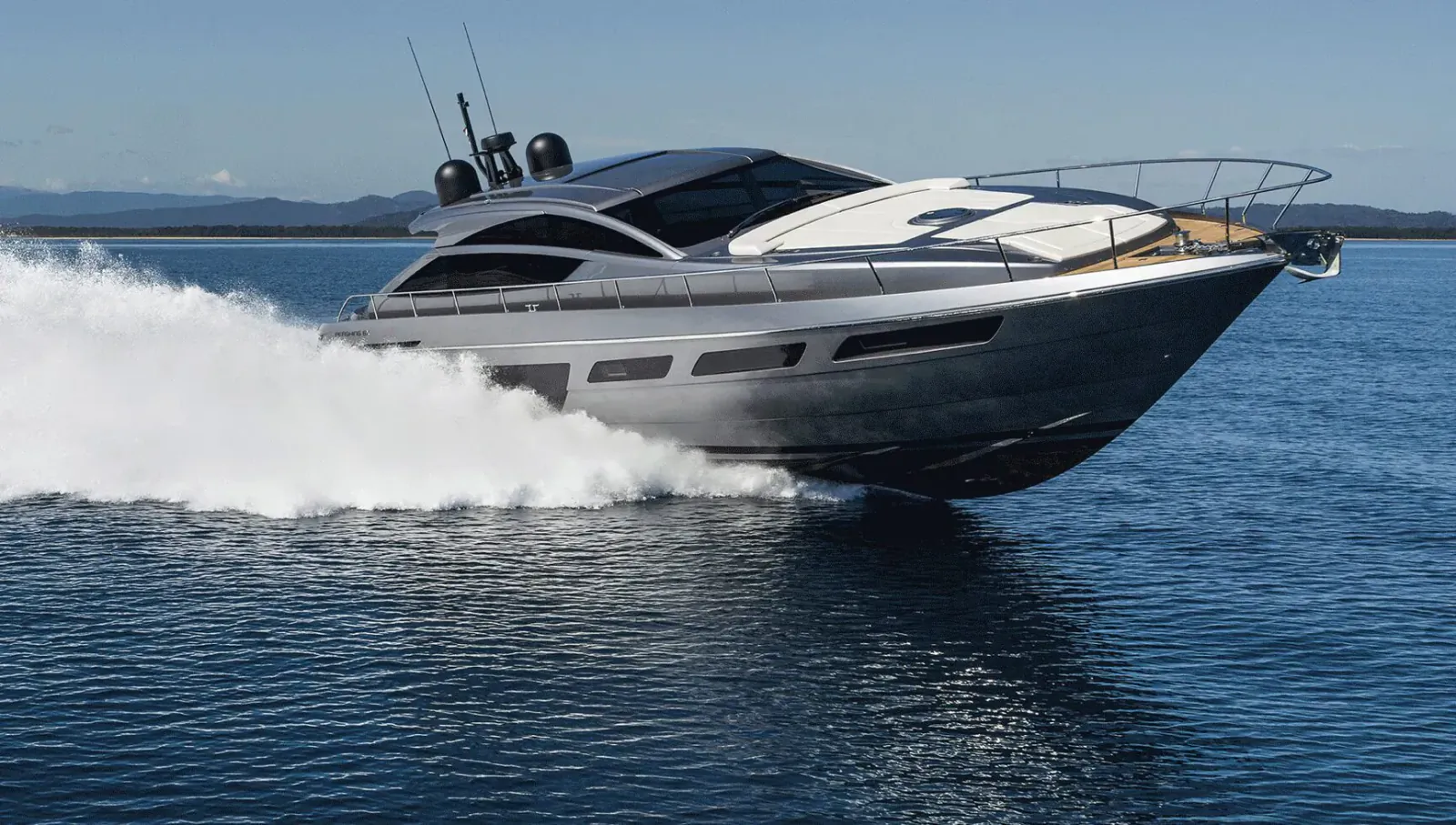 Silver Ferretti Yachts 720 luxury motor yacht speeding on blue water with white wake, mountains in background.