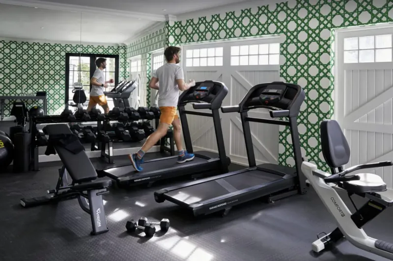 Modern hotel gym with green patterned walls: man running on treadmill, another on elliptical, weights and recumbent bike.