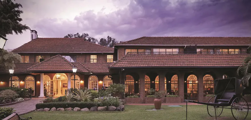 Fairmont The Norfolk Nairobi hotel exterior at dusk with terracotta roofs, lit arches, gardens, and palm trees.