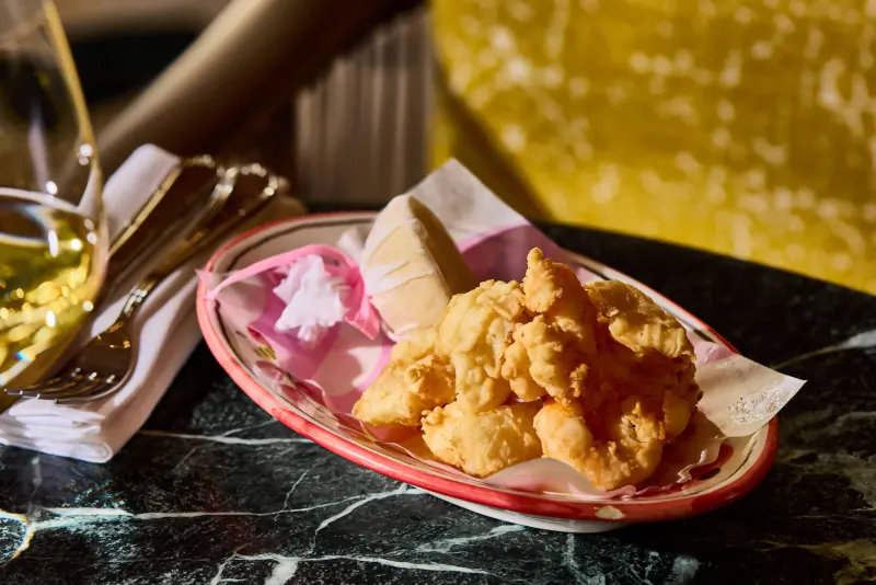 Fried shrimp on pink napkin in oval dish with cheese, napkin, wine glass, and silverware on marble table at Italian restaurant
