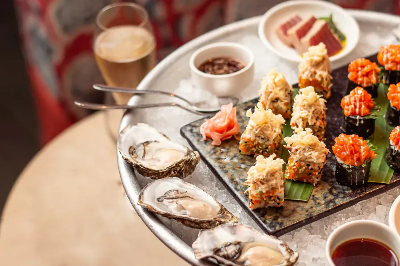 Assortment of sushi rolls, oysters on ice, and Champagne on a round tray