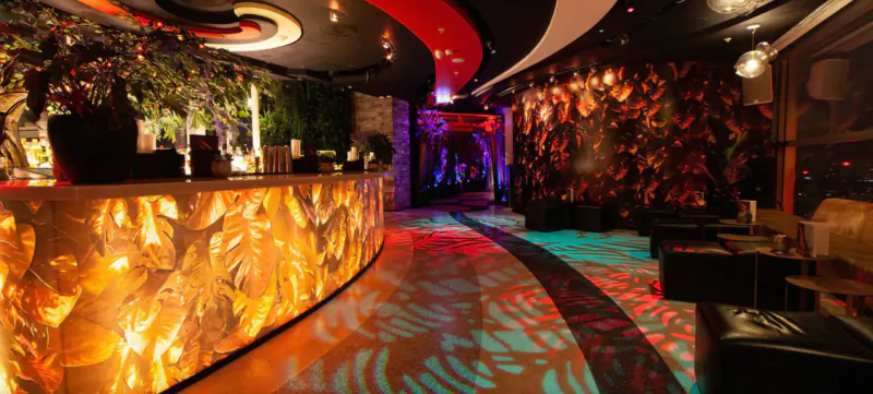 Sushi Samba gallery: curved glowing orange bar, neon-lit lounge with plants, red seating, and vibrant floor patterns