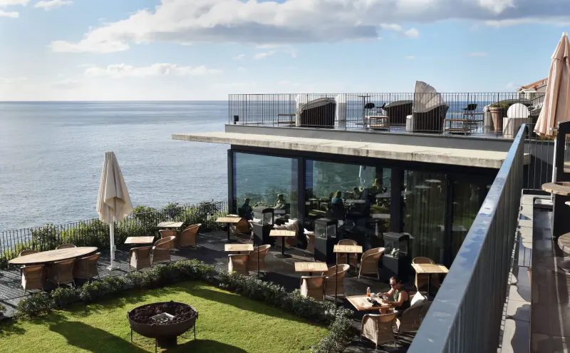 Outdoor terrace at Les Suites Hotel at The Cliff Bay, Funchal, Madeira, with ocean views, lounge seating, umbrellas, and patrons.