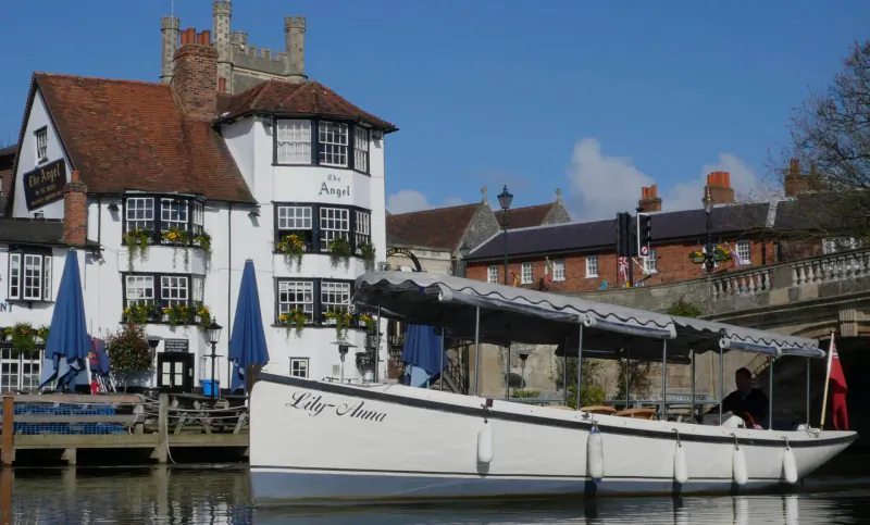 White boat 'Lady Ann' moored at Hobbs of Henley pub by river, with blue umbrellas and stone bridge.