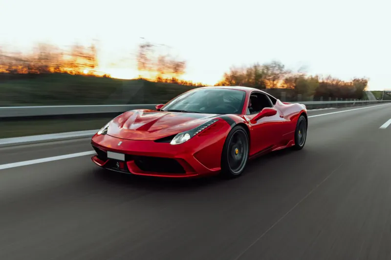 Red Ferrari 488 speeding on highway at sunset with autumn trees lining the road