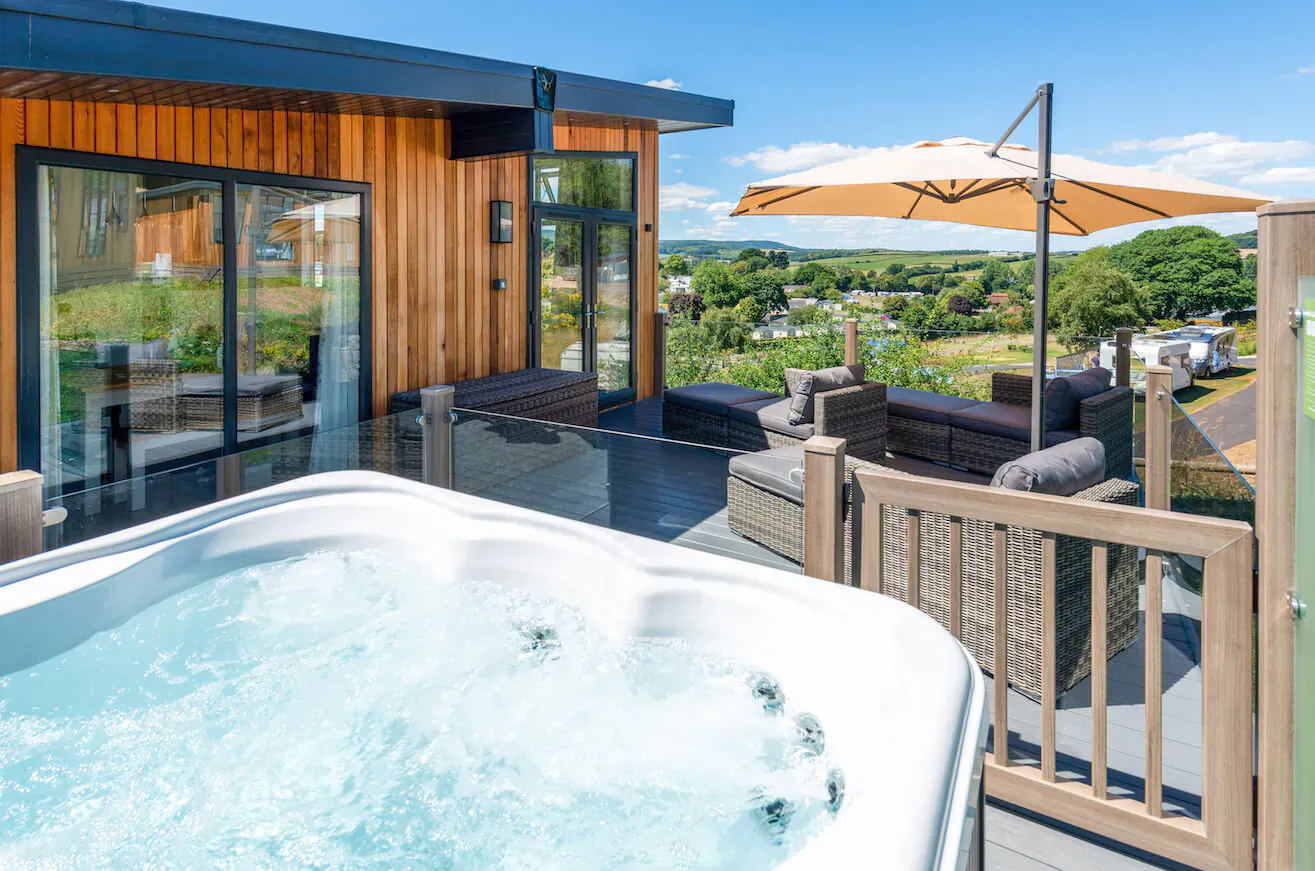 Cofton Luxury Lodge deck with bubbling hot tub, outdoor seating, and scenic Devon countryside view.