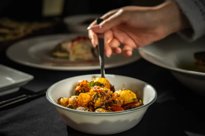 Hand spooning spicy cumin potato curry garnished with cilantro from white bowl on table at Mint Leaf London
