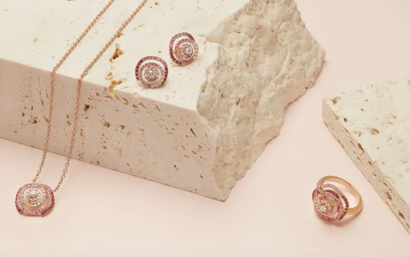 Rose gold seashell jewelry set with pink gems: necklace, stud earrings, ring on white textured stone surface