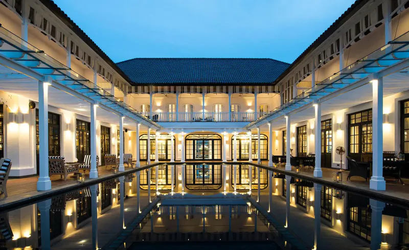 The Sanchaya luxury resort courtyard with central pool reflecting lit colonial-style buildings at dusk